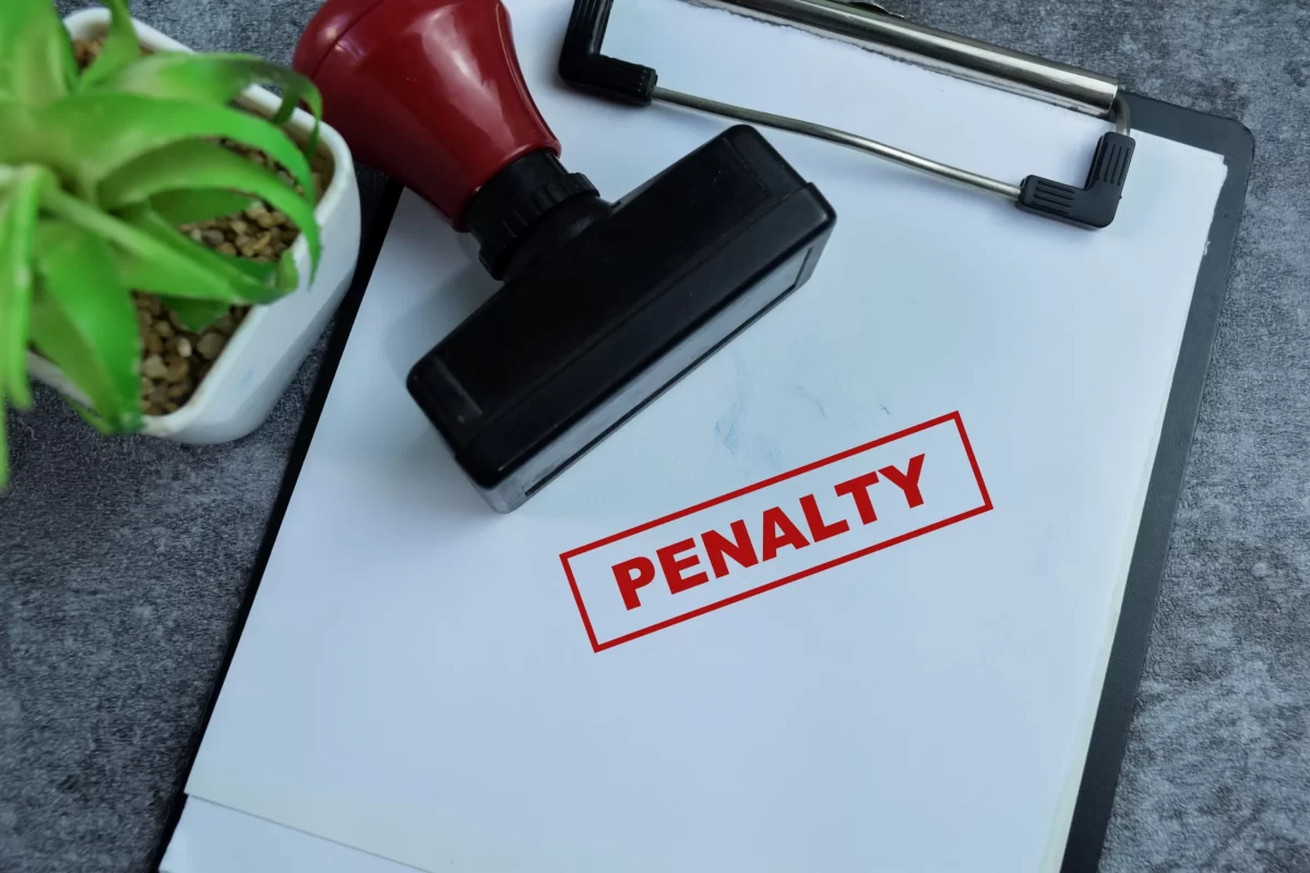 Red PENALTY stamp on paperwork beside a rubber stamp and small plant.